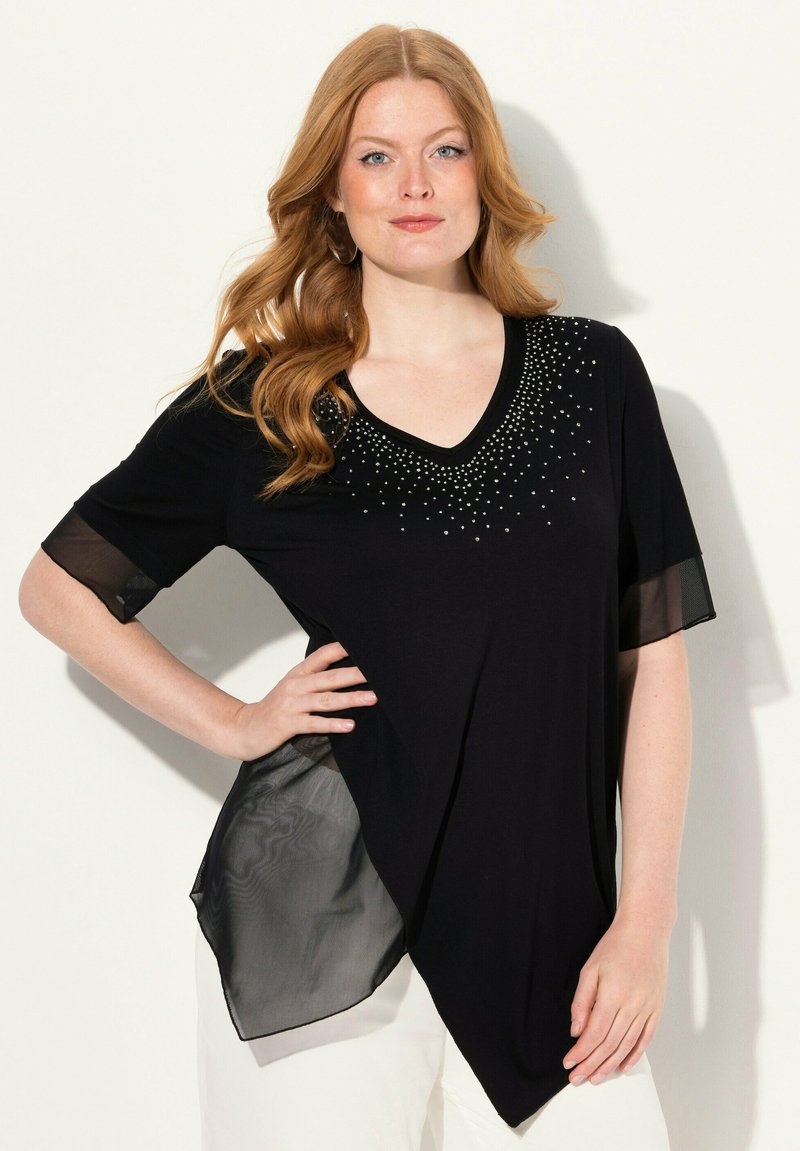 Haut noir avec un col en V et de courtes manches en maille transparente. Présente des embellissements en perles le long de l'encolure et un ourlet asymétrique.