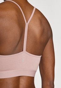 Ανοιχτό ροζ αθλητικό σουτιέν με λεπτές τιράντες, ριμπ ύφανση και μικρό λογότυπο στο πίσω μέρος. Διαθέτει ομαλό, εφαρμοστό σχέδιο.