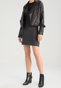 Mustapaitainen moottoripyöräjacket harmaassa hihattomassa mekossa, jossa on pitsiyksityiskohta. Mustat nilkkakengät, joissa on korokepohja, täydentävät asukokonaisuutta.