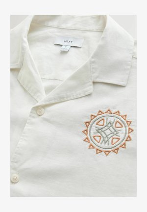Short-sleeve shirt in light cream fabric, featuring a collar, button closure, and a circular embroidered design in green and orange.