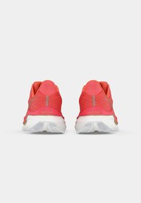 Een paar koraalrode hardloopschoenen met witte zolen, gezien vanaf de achterkant op een plain witte achtergrond.