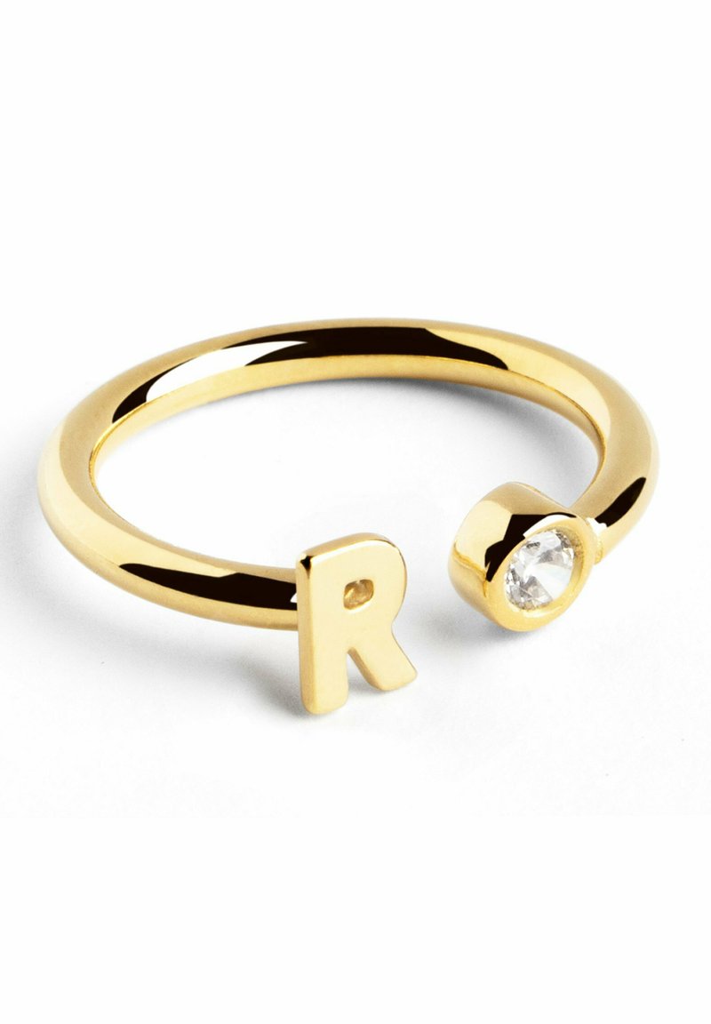 Anello regolabile in tono oro con la lettera maiuscola "R" e una pietra preziosa trasparente, dalla forma elegante e dalla finitura lucida.