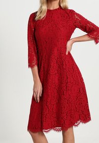 Punainen pitsimekko kolme neljännesosaa hihoilla, aaltoilevalla helmalla, kukkakuviolla ja tiiviillä vartalolla, jossa on läpinäkyvä pitsipinta kauttaaltaan.