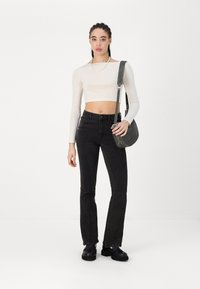 Jeans de ganga pretos com um corte slim e ligeiramente evasé, combinados com uma blusa de manga longa cropped branca. Bolsa cinza com alça de ombro. Sapatos pretos.