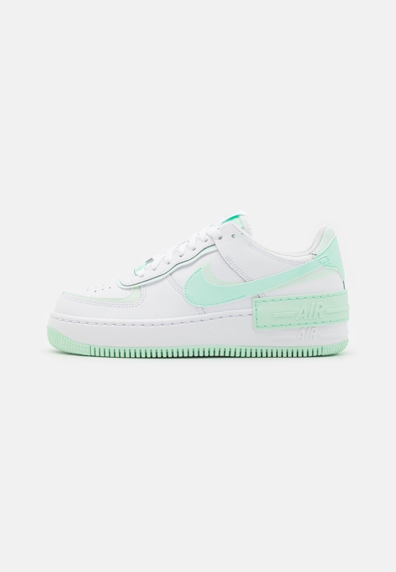 Baskets basses blanches avec semelle vert menthe, logo Nike et accents au talon, avec perforations et lacets sur fond uni.