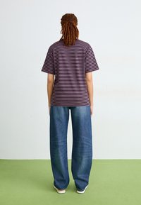 T-shirt a righe a maniche corte di colore viola scuro e rosa, abbinato a jeans a gamba larga blu. Tessuto morbido con una vestibilità rilassata, mostrato da dietro.