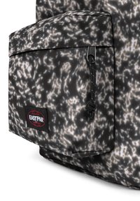 Musta ja harmaa kuviollinen reppu, jossa on vetoketjullinen etutasku ja musta Eastpak-logo. Teksturoitu kangas tarjoaa kestäväisyyttä.