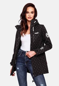 Black waterproof jacket featuring a dot pattern, hood, zippered chest pocket, and logo accents. Paired with blue jeans.