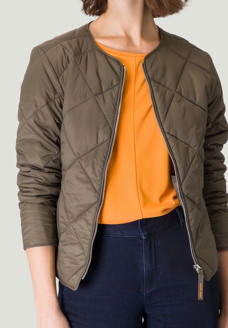 Veste bomber matelassée olive en tissu léger, col rond, fermeture éclair, et poignets côtelés, superposée sur un haut orange.