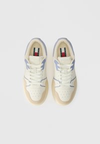 Tennarit, joissa on kermanvärinen nahkainen päällinen vaalean liiloin yksityiskohdin, rei'itetty varvas, beigestä mokkanahasta tehdyt päällysteet ja vaaleanruskea kumipohja.