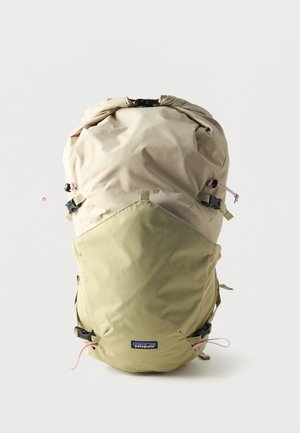 Zaino Patagonia beige chiaro e verde oliva con chiusura a rotolo, spallacci regolabili e logo del marchio frontale su sfondo uniforme.