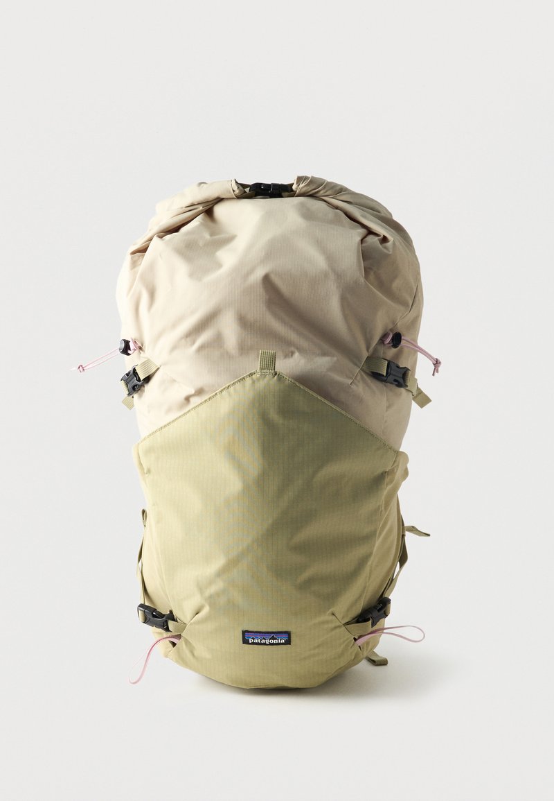 Mochila Patagonia en beige claro y verde oliva con cierre enrollable, correas ajustables y logo de la marca en la parte frontal sobre un fondo liso.