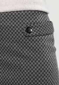 Tejido de patrón de espiga tejido en negro y gris; cuenta con un botón negro de acabado mate en la cinturilla.