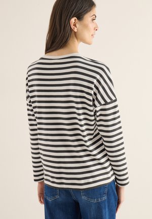 Czarna i biała koszulka w paski z długim rękawem, o luźnym kroju i zaokrąglonym dekolcie, zestawiona z niebieskimi dżinsami. Tkanina o fakturze.