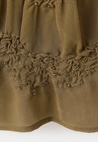 Tissu brun texturé avec des sections froncées décorées de petites perles métalliques formant un motif décoratif près du bord inférieur.