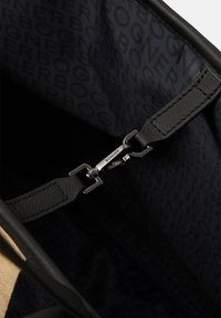 Interno di una borsa in pelle nera con chiusura a zip, caratterizzato da una fodera in tessuto stampato con logo in tonalità scure e un dettaglio con clip metallica.