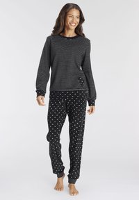 Black and white striped long-sleeve top with crew neck and pocket, paired with black pants featuring white heart pattern and ribbed cuffs.