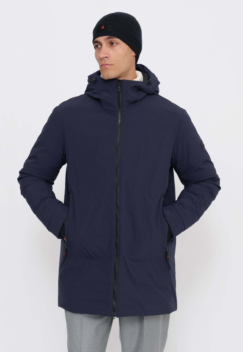 Giacca imbottita lunga blu navy con zip frontale, cappuccio e tasche laterali. Tessuto morbido con coulisse regolabili e dettagli hardware minimali.