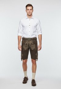 Braune Lederhosen-Shorts mit gestickten Motiven, kombiniert mit einem weißen Hemd mit Knöpfen, knielangen Socken und dunklen Schuhen.