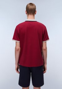 T-shirt rossa a maniche corte con colletto beige e blu, realizzata in cotone, presenta una vestibilità comoda e un design semplice, abbinata a pantaloni corti blu.