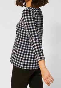 Navy and white checked long-sleeve top in a loose fit, featuring a round neckline and soft fabric with a textured finish.