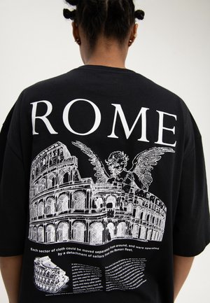 Osoba nosząca czarną koszulkę z białymi szkicami Koloseum Rzymskiego, skrzydlatym cherubem i dużym tekstem "ROME" na plecach.