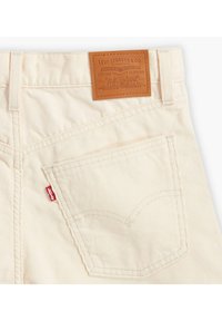 Kermanväriset samettihousut, joissa nahkainen merkki kohokuvioidulla tekstillä, punainen lappu takataskussa ja hienovarainen poimutettu kuvio.