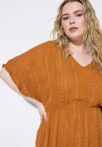 Lässiges, V-Ausschnitt-Kleid aus rostorangefarbenem Stoff mit strukturierten Streifen und glitzernden Akzenten. Kurze Ärmel, taillierte Taille und flatternder Rock.