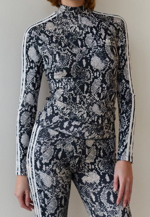 Žena v černo-bílém roláku s hadím vzorem a odpovídajícími legínami s bílými pruhy na rukávech a nohavicích.