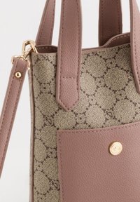 Beige canvasväska med en strukturerad bas i rosa läder, utrustad med ett guldtrycklås och dekorativa sömmar på utsidan.