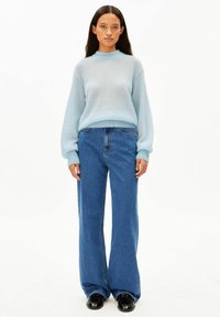 Hellblauer Strickpullover mit Rundhalsausschnitt und Ballonärmeln, kombiniert mit hoch taillierten, weit geschnittenen blauen Jeans. Schwarze Schuhe vervollständigen das Outfit.