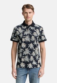 Polo de manga corta en azul marino con un patrón de hojas de palma en beige claro y azul. Presenta un cuello con solapa y una tela texturizada.