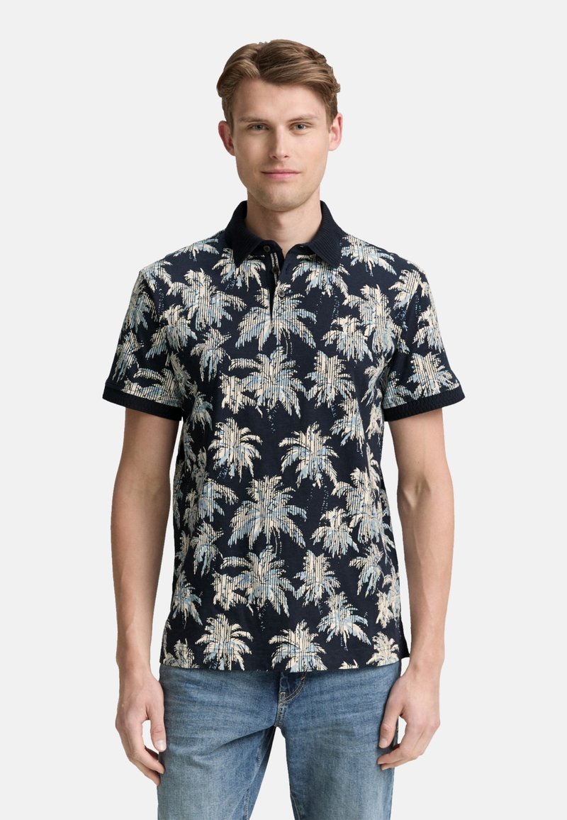 Polo de manga corta en azul marino con un patrón de hojas de palma en beige claro y azul. Presenta un cuello con solapa y una tela texturizada.