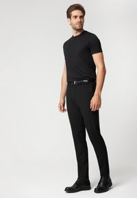 Czarna koszulka z krótkim rękawem, zestawiona z czarnymi spodniami i czarnymi sznurowanymi botkami do kostki. Gładki materiał o dopasowanym kroju i prostym sylwetce.