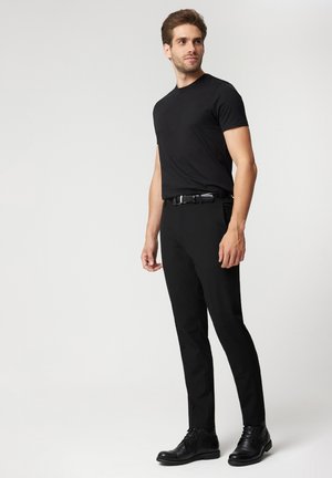 Czarna koszulka z krótkim rękawem, zestawiona z czarnymi spodniami i czarnymi sznurowanymi botkami do kostki. Gładki materiał o dopasowanym kroju i prostym sylwetce.