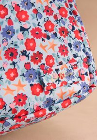 Material cu model floral cu flori roșii, mov, roz și stele portocalii; eticheta materialului are inscripția „Cath Kidston” în scris aurit.