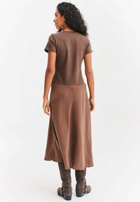Brązowa sukienka z krótkim rękawem o zwiewnej sylwetce, sięgająca do połowy łydki. Miękka, gładka w dotyku, z prostym tyłem i bocznym rozcięciem.