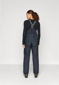 Sötétkék h�ózokni állítható pántokkal, cargo zsebekkel és vízálló anyaggal. Fekete hosszúujjú póló fölött viselve.