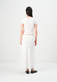 White fitted t-shirt and long white skirt, both with a smooth texture. Black lace-up shoes visible at the bottom. Neutral background.