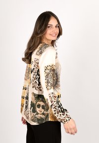 Long-sleeve blouse featuring a light beige fabric with various graphic prints, including leopard patterns and artistic illustrations.