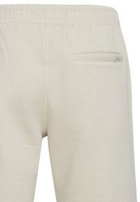 Pantalones de chándal color crema, hechos de una tela suave, con una cinturilla elástica, un bolsillo trasero y detalles de diseño minimalistas.