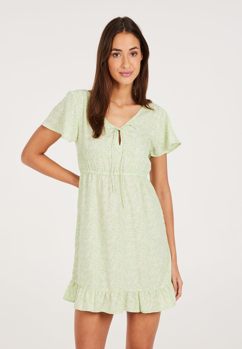 Kurzes grünes Kleid mit kurzen Wellenärmeln, einem V-Ausschnitt, Kordelzugdetails in der Taille und einem Rüschensaum. Überall mit floralem Muster.