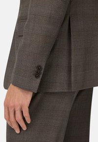 Maniche di giacca da completo a quadri marrone con tre bottoni scuri, tessuto texture e vestibilità sartoriale con una apertura sul retro.