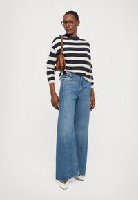 Pull en tricot rayé bleu marine et crème, jeans en denim bleu à jambes larges, escarpins crème à bout pointu, et sac à main marron avec bandoulière.