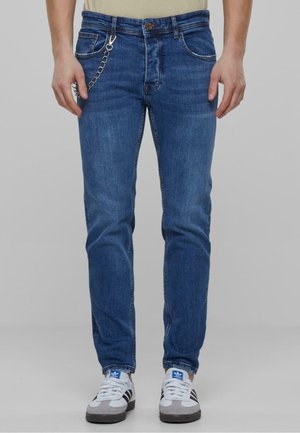 Dark blue denim jeans with a slim fit, five-pocket design, metal hardware accents, and a chain detail attached to the front.