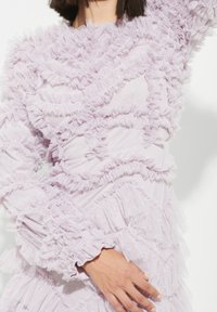 Ljuslila klänning med lager av volanger i genomskinligt tyg, med en strukturerad yta och utspridda stjärnmönster.