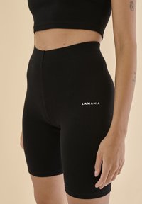 Černé žebrované šortky s těsným střihem, mají středně vysoký pas a malé bílé logo "LAMANIA" po straně.