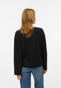 Melnas krāsas garām piedurknēm topi ar vaļēju piegriezumu, apaļu kakla izgriezumu un nedaudz īsāku apakšmalu. Saskaņots ar gaiši ziliem džinsa džinsiem.