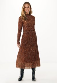 Robe à manches longues et col haut en orange-brun avec un imprimé léopard noir ; taille cintrée, jupe fluide, accompagnée de bottes noires jusqu'aux genoux.