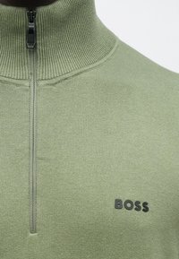 Sweter dziany w jasnozielonym kolorze z półzamek kołnierzem. Posiada teksturowaną powierzchnię i czarne logo BOSS na piersi.